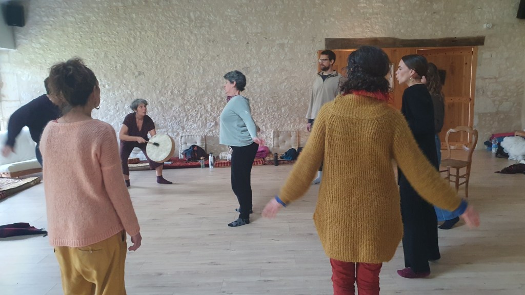 A group of people in a dance studio, some dressed in loose clothing, gather to practice a form of contemporary dance. The ...